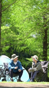 新緑のキャンプ場で椅子に座る笑顔のアウトドアやレジャーを楽しいミドルの夫婦　鳥や景色を眺める縦動画　指を差して見つめる　スローモーション