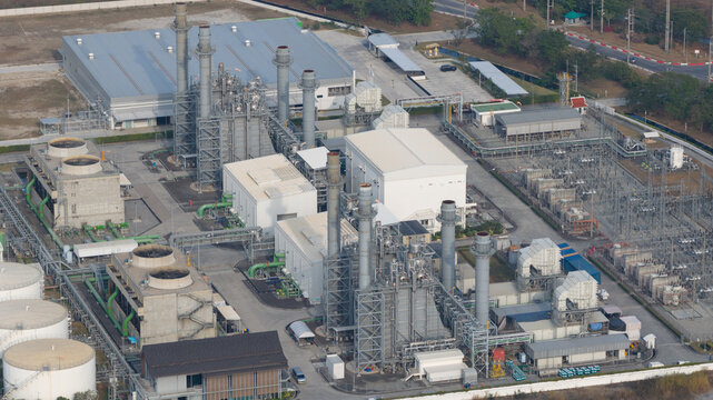Aerial view of a large industrial power plant facility featuring smokestacks, cooling towers, and electrical substation infrastructure under clear daylight in Rayong, Thailand.