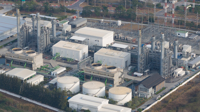 Aerial view of a large industrial power plant facility with cooling towers, storage tanks, and an electrical substation in Rayong, Thailand.