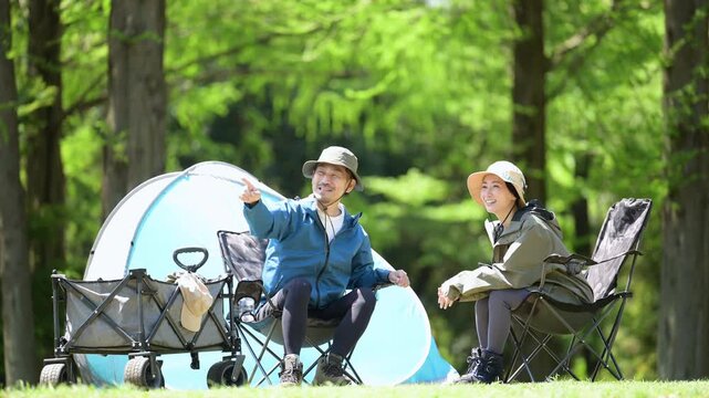 新緑のキャンプ場で椅子に座る笑顔のアウトドアやレジャーを楽しいミドルの夫婦　鳥や景色を眺める動画　指を差して見つめる