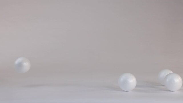White Polystyrene Balls Bouncing and Rolling Across a Plain Studio Surface