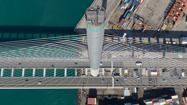 Aerial view of Stonecutters Bridge showing the massive cable-stayed tower, highway traffic, and shipping containers in New Territories, Hong Kong.