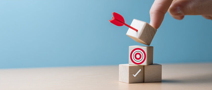 hand pushing wooden blocks with a checkmark icon towards a goal target on a blue background.