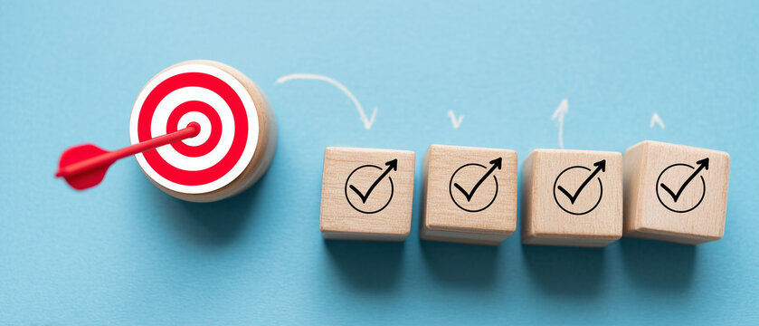 hand pushing wooden blocks with a checkmark icon towards a goal target on a blue background.