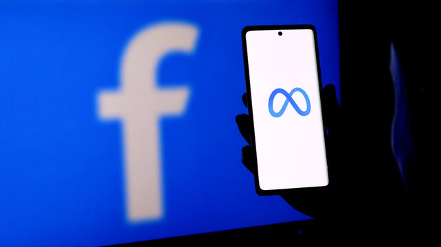 A person holding a smartphone displaying the meta logo in front of a facebook logo screen
