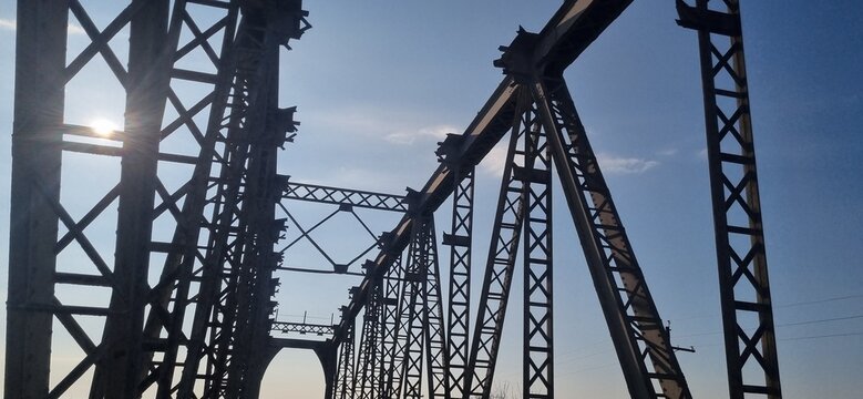 looking up at intricate iron structures of a railway bridge against a blue sky.
