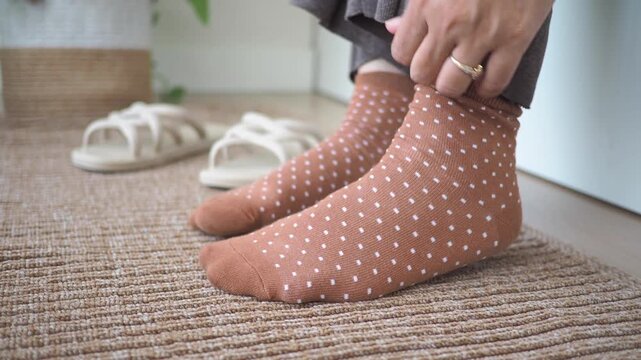 Woman pulling up polka dot socks over her ankles during morning routine.