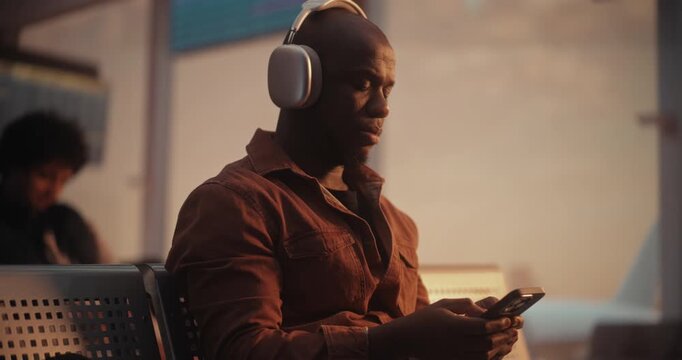 While Waiting For Flight, Focused African American Passenger Uses Mobile Device to Send Messages, Coordinating Business Details or Checking in With Contact. Efficiency of Modern Digital Traveler.