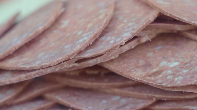 Sliced beef salami stacked in pile rotating slowly closeup view of processed meat product.