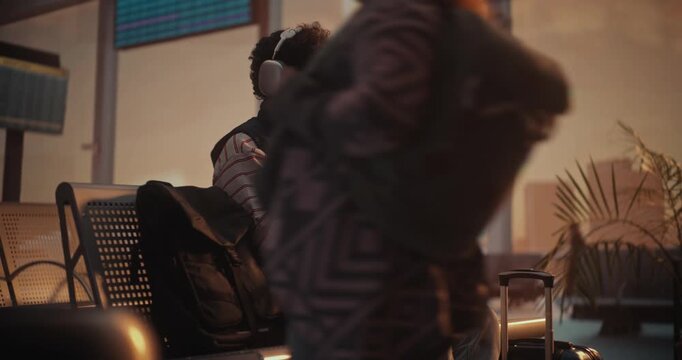 Focused Young Man in Striped Sweatshirt Putting on Large Over Ear Headphones. Male Uses Smartphone to Scan Yellow Paper Ticket, Instantly Pulling Up Digital Version on Screen to Verify Flight Details.