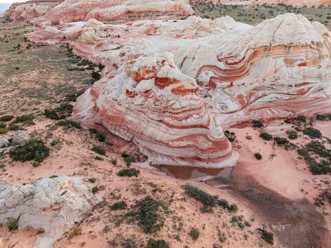 Aerial view of the unique White Pocket sandstone formations with red swirls and desert vegetation in Coconino County, Arizona, United States.
