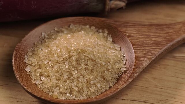Cane sugar crystals on a wooden spoon with sugarcane
