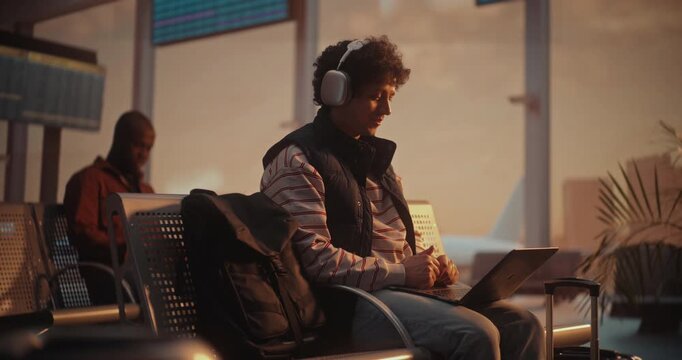 Young Professional Having Business Video Call at Airport with Plane Departing Behind. Young Man With Curly Hair Engages in Important Business Meeting Via Laptop. Concept of Global Communication.