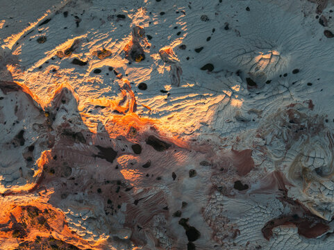 Aerial view of White Pocket rock formations with swirling sandstone textures and small water pools under golden light Coconino County, Arizona, United States.