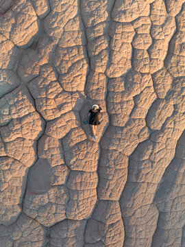 Aerial view of White Pocket with a woman lying on the unique cracked sandstone formations under warm golden light in Coconino County, Arizona, United States.