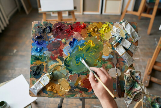 An artist mixing colorful oil paints on a wooden palette with a brush in a creative art studio