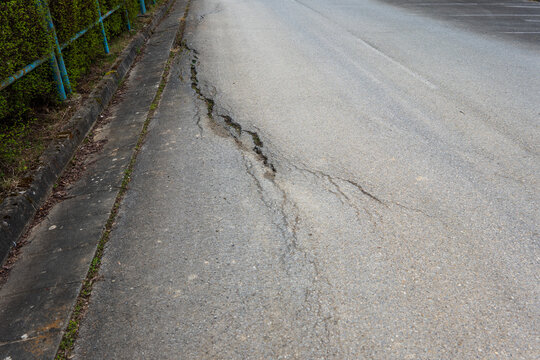 Damaged asphalt road with cracks and deteriorated surface near curb, infrastructure problem and road maintenance concept.
