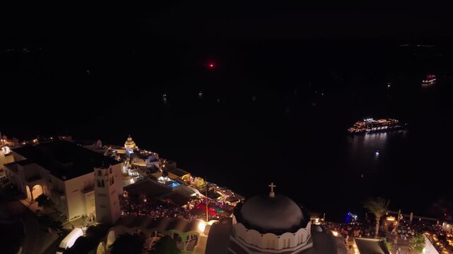Night reveal of Fira's glowing white architecture, transitioning to the dark caldera where a fireworks display simulates a volcanic eruption at the Ifaisteia festival.