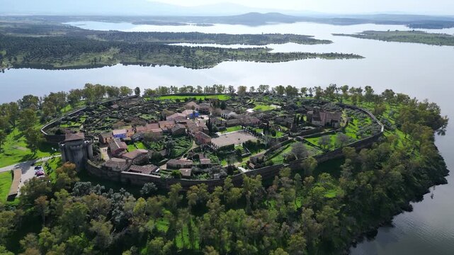Aerial drone view of Granadilla medieval walled village in Extremadura, Spain, surrounded by reservoir landscape with water and countryside.
