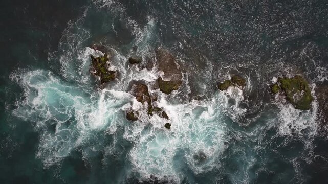 Top-down drone shot of waves surging around San Mateo Rocks in San Clemente, California, creating bright white sea foam patterns over dark offshore boulders in the Pacific Ocean.