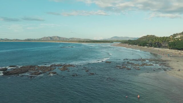 Drone pan left over Tamarindo coastline with waves and beach under bright sunlight and clear tropical weather.