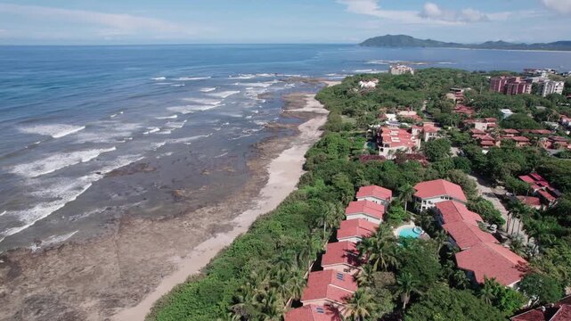 Drone pan right over Playa Langosta coastline with waves and rocky shore under bright sunlight and clear weather.