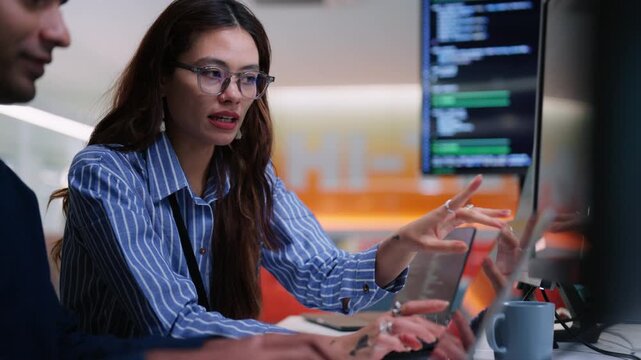 Mentor explaining work to new colleague in tech company, multiple screens on desk, teamwork, onboarding, collaboration, training, digital workplace, modern office environment, innovation