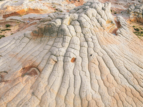 Aerial view of White Pocket rock formations featuring unique brain-like textures and a person standing on the sandstone in Coconino County, Arizona, United States.