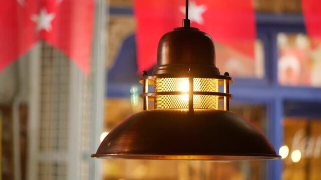 Industrial style copper hanging lamp glowing in cafe with blurred turkish flags background.