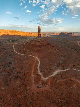Aerial view of the sandstone spires and winding dirt roads of the Valley of the Gods under a blue sky with scattered clouds in San Juan County, Utah, United States.