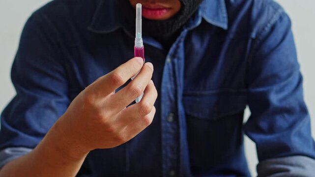 Close up of kidnapper wearing balaclava holding needle with pink fluid