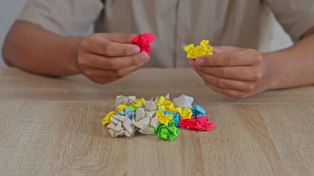 Close-up of hands with OCD sorting and stacking colorful crumpled paper balls on wooden desk