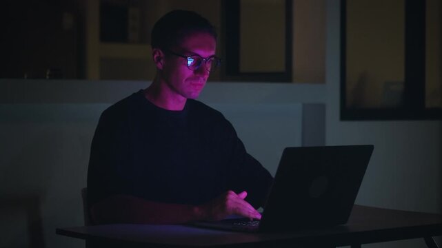 Man using laptop at night, illuminated by screen light and focused on digital tasks. Technology lifestyle reflects daily tech usage, connectivity, smart living and modern digital habits