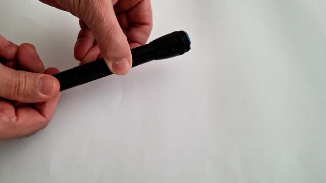 Hands hold black flashlight body and end cap on white surface, demonstrating assembly, inspection, or repair of portable lighting device in a clear instructional context