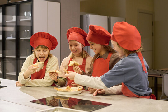 Caucasian children sharing pizza during cooking class in kitchen, learning teamwork and food preparation. Suitable for education, kids lifestyle, culinary program promotion