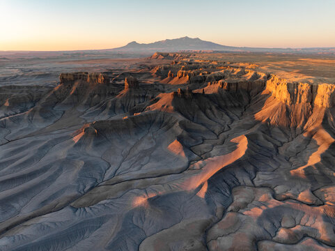 Aerial view of the rugged badlands and eroded rock formations under golden hour light near the Henry Mountains in Hanksville, Utah, United States.
