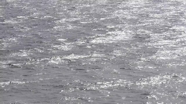 Close-up footage of rippling water surface with shimmering sunlight reflections. Natural abstract background with dynamic wave motion, ideal for overlays, cinematic scenes, and environmental concepts.