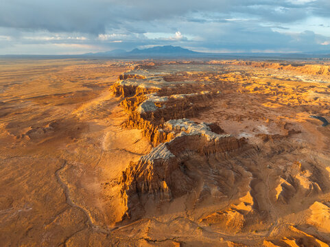 Aerial view of Goblin Valley State Park showing sandstone hoodoos, a prominent rocky ridge, and distant mountains under an orange sunset sky Green River, Utah, United States.