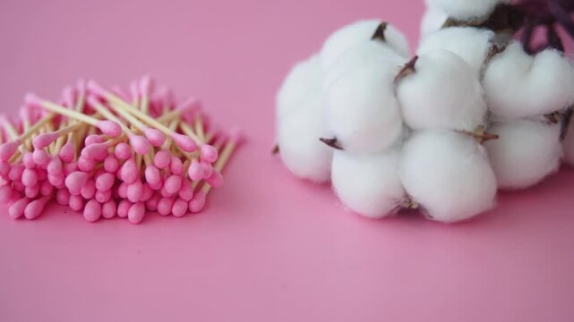 Pile of pink cotton swabs near white cotton bolls on pink background.
