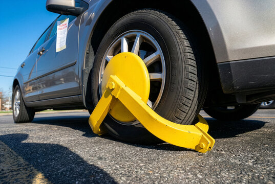 A silver car immobilized by a bright yellow wheel clamp with a parking violation notice on the window.