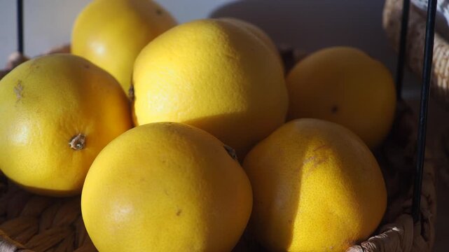 Fresh pomelo fruits in basket on sunlit table creating warm light and shadow.