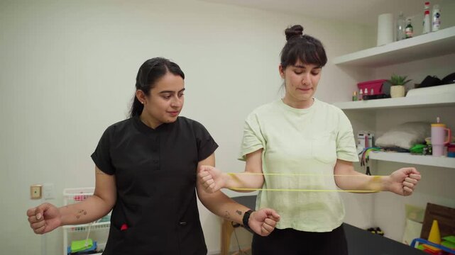 Physiotherapist guiding a patient performing shoulder external rotation exercises with a resistance band to strengthen her rotator cuff and improve joint stability
