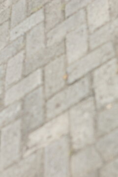 Blurred texture of grey interlocking paving blocks on a pedestrian walkway.