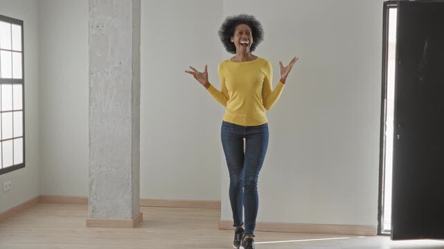 Woman with arms outstretched and smiling, crossing legs while dancing in studio doorway; joy celebration.