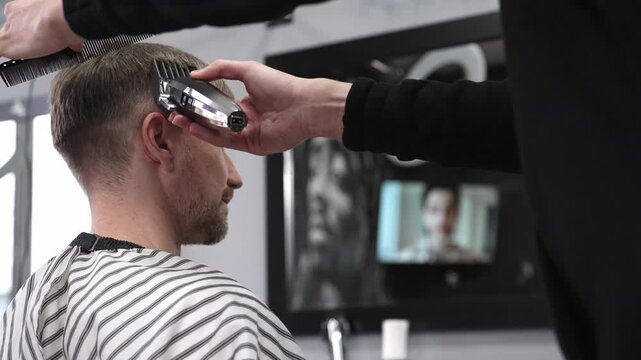 Professional barber trimming male client's hair using electric razor, creating precise haircut in contemporary barbershop setting with sleek styling tools