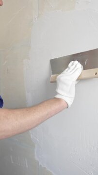 Unknown female construction worker wearing protective gloves applying plaster, smoothing wall surface during home renovation work, vertical view