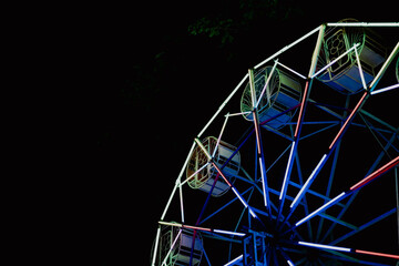 Ferris wheel amusement park night neon light carnival ride Ferris wheel structure glowing with neon light night, colorful metal frame and gondola against dark sky, amusement park carnival ride © Thitongpi