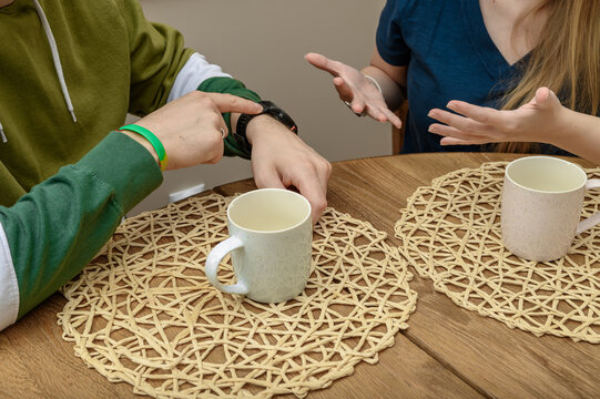 A couple of people, a man and a woman, sitting at a table in a restaurant. The man is pointing at his watch, he is late for a meeting.