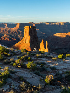 Aerial view of Canyonlands National Park featuring red rock buttes and people standing on a cliff edge during golden hour in Utah, United States.
