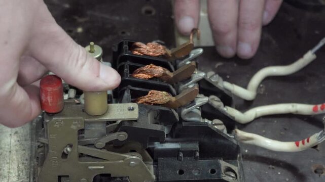An electrician's hands work with a disassembled electric starter. Repair of an old-style three-phase automatic machine with copper winding contacts